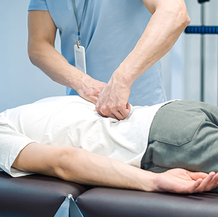 A chiropractor performing a manual spinal adjustment on a patient lying face down on a treatment table.