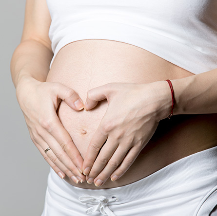 A pregnant woman forms a heart shape over her belly, representing prenatal chiropractic care and maternal wellness.